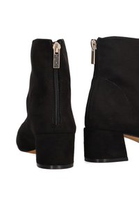 Botas de ante negras hasta el tobillo con un tacón grueso, con cremallera lateral y textura suave. Diseño minimalista sin patrones o acentos visibles.