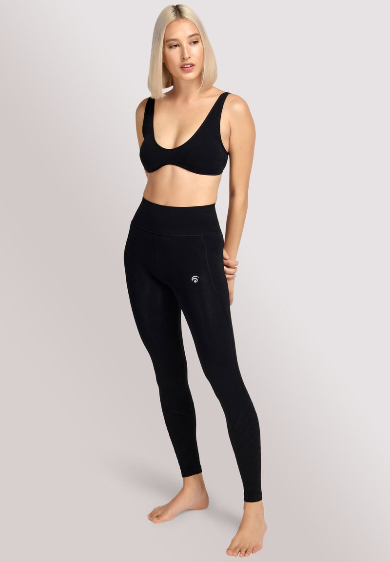 Soutien-gorge de sport noir et leggins taille haute en tissu lisse et extensible. Les leggins comportent un petit logo sur le côté.