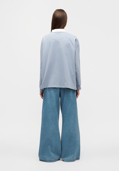 Ανοιχτό μπλε πουκάμισο με μακριά μανίκια και λευκό γιακά, συνδυασμένο με τζιν παντελόνι με φαρδιά μπατζάκια. Το σύνολο έχει άνετη εφαρμογή και απαλό υλικό.