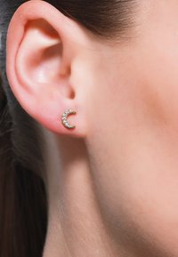 Orecchini a forma di mezzaluna in oro, impreziositi da piccoli brillanti, indossati su un orecchio. Finitura metallica liscia con accenti scintillanti.
