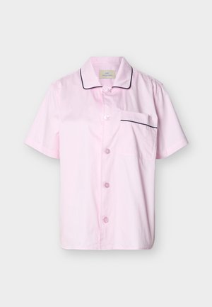 Chemise à manches courtes rose clair boutonnée avec passepoil noir sur le col et la poche, présentée sur un fond clair uni.