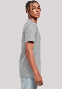 Ljusgrå kortärmad t-shirt i bomullsblandning, med rund hals och avslappnad passform, visas på en modell från sidan.