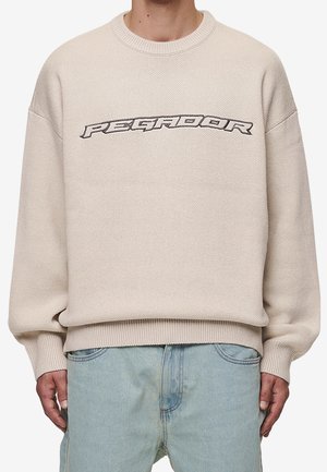 Suéter de punto crema con cuello redondo, tejido texturizado y puños acanalados, con el logo "PEGADOR" en gris oscuro en el pecho.