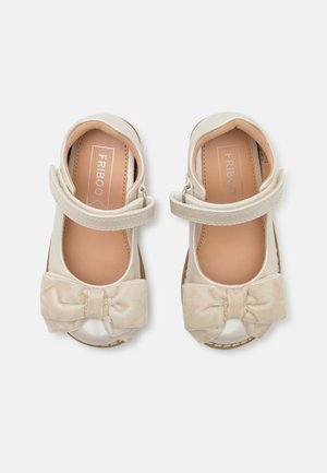 Cremefarbene Kleinkindschuhe mit Klettverschlüssen und großen Stoffschleifen an den Zehen, nebeneinander auf weißem Hintergrund präsentiert.