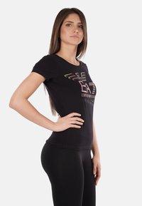 T-shirt nera a maniche corte con design aderente, caratterizzata da una stampa logo colorata sulla parte anteriore e in tessuto morbido e elasticizzato.