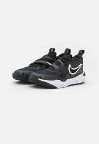 Chaussures de sport noires avec tige en mesh, fermeture à double sangle et accents blancs. Présente une semelle texturée pour l'adhérence et des languettes de traction à l'arrière.
