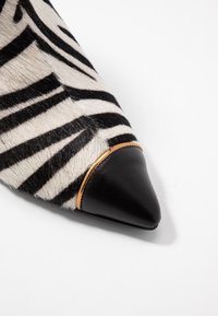 Puntige schoen van zwart-wit gestreepte bont, met een zwarte leren neus en een dunne gouden accent rond de kraag.