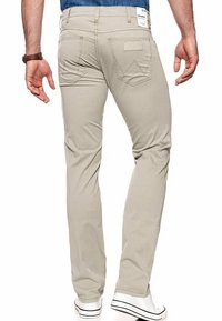 Lichtbeige katoenen broek met rechte pasvorm, voorzien van twee achterzakken en witte stiksels, gecombineerd met witte sneakers.