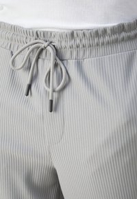 Lichtgrijze geribbelde joggerbroeken met een elastische tailleband, verstelbaar trekkoord en zwarte uiteinden. Voorzien van zijzakken.