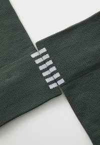 Gröna stickade tröjärmändar med ett mönstrat textur. Vita accentstrimmor på den ena ärmen. Närbild som framhäver detalj och material.