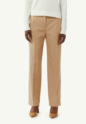Beige maßgeschneiderte Hose mit glatter Textur, geradem Bein und vorderer Bügelfalte, kombiniert mit hellbraunen High-Heels.