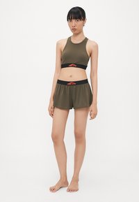 Olive green sports bra and matching shorts, both made of smooth fabric. Bra features black and red branded elastic band; shorts have similar waistband.