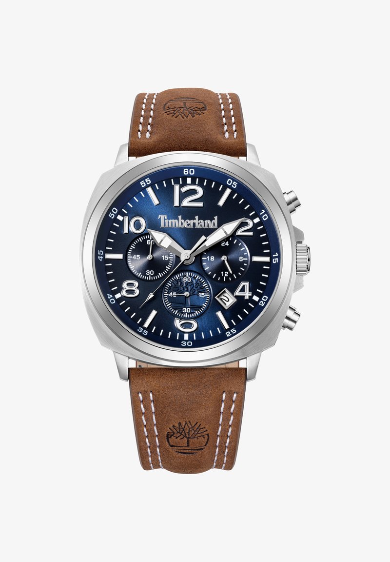 Brūna ādas siksna pulkstenis ar sudraba metāla korpusu, tumši zils ciparnīca, lieli skaitļi un hronogrāfa subciparnīcas. Redzams Timberland logo.