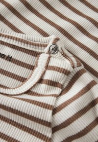 Primer plano de una prenda de rayas en crema y marrón con textura acanalada, con un botón de presión de metal en la costura del cuello.