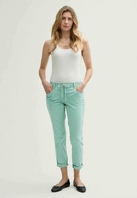 Mintgröna byxor med dragsko i midjan, med sidofickor och uppvikta muddar, kombinerade med en vit linne och svarta ballerinaskor.