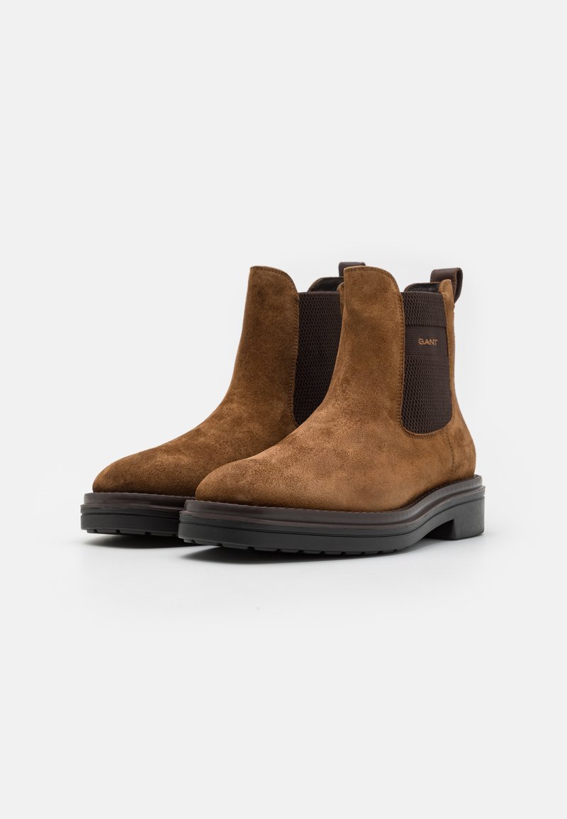 Bottes Chelsea en suedine marron avec des panneaux latéraux élastiques, un bout arrondi et une semelle noire épaisse. Branding minimal sur le panneau latéral.