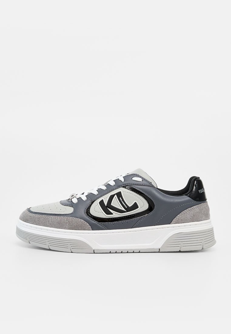 Zapatilla baja en gris, negro y blanco con detalles en ante, cordones blancos y un logo "KL" en el panel lateral.