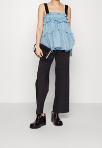 Top senza maniche blu chiaro con strati arricciati, bretelle nere; abbinato a pantaloni larghi neri e scarpe nere con tacco. Tiene in mano una piccola borsa nera.