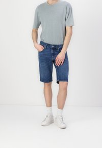 Světlé šedé bavlněné tričko ve spojení s tmavě modrými riflovými šortkami. Šortky mají rovný střih a viditelné švy. Look doplňují bílé tenisky.