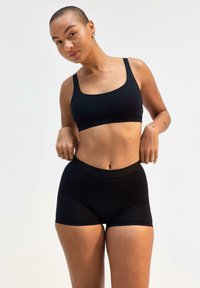 Set di reggiseno sportivo e pantaloni corti neri, realizzato in tessuto morbido. Il reggiseno presenta spalline larghe; i pantaloni corti hanno un cinturino elastico e una silhoutte aderente.