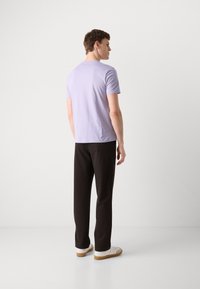 T-shirt violet clair à manches courtes associé à un pantalon marron foncé. Le t-shirt a une coupe classique et un tissu doux, porté avec des chaussures blanches.