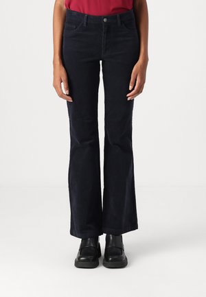 Navy corduroy flared pants with front and back pockets, zipper fly, and a fitted waist, paired with black chunky shoes, viewed from the front.