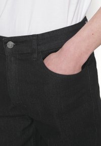 Vaqueros de mezclilla negros con una textura suave y un corte ajustado. Presentan un botón de metal, un bolsillo frontal y costuras discretas a lo largo de las costuras.