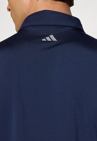 Polo-shirt marine avec un col structuré, fabriqué dans un matériau lisse. Présente un accent de logo gris dans le dos, près de l'encolure.