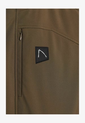 Chaqueta verde oliva con un bolsillo en el pecho con cremallera y un parche negro con un diseño geométrico blanco. Tejido suave con un acabado mate.