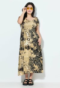 Robe maxi à imprimé animal avec un corsage froncé, dans des teintes dorées, noires et beiges. Associée à des sandales à plateforme noires et des lunettes de soleil jaunes.