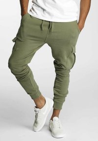 Oliwkowe joggery cargo z tapered nogawkami, elastycznym pasem i bocznymi kieszeniami. W zestawie z białymi trampkami, z sznurówkami i logo.