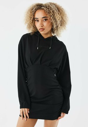 Robe noire à capuche en tissu doux, dotée de manches longues, de côtés froncés et d'un cordon de serrage à la capuche. Design minimaliste sans motifs.