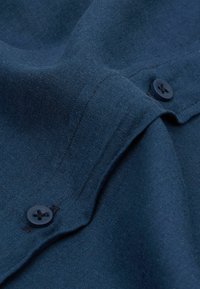 Marinblått tyg med en slät yta, prytt med två svarta knappar och synlig sömnad. Materialet ser något skrynkligt ut.