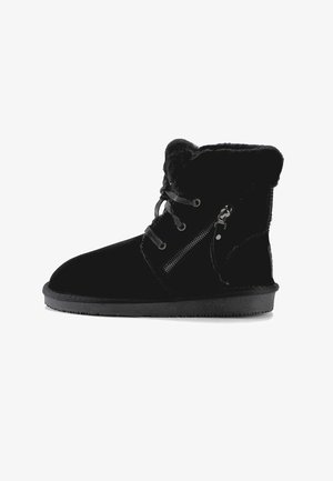 Bota negra de invierno con forro de piel, cordones delanteros, cremallera lateral y suela plana de goma, diseñada para clima frío.