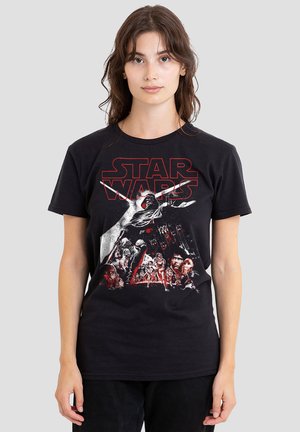 Young woman wearing black Star Wars graphic T-shirt showing multiple characters and logo on light gray background.