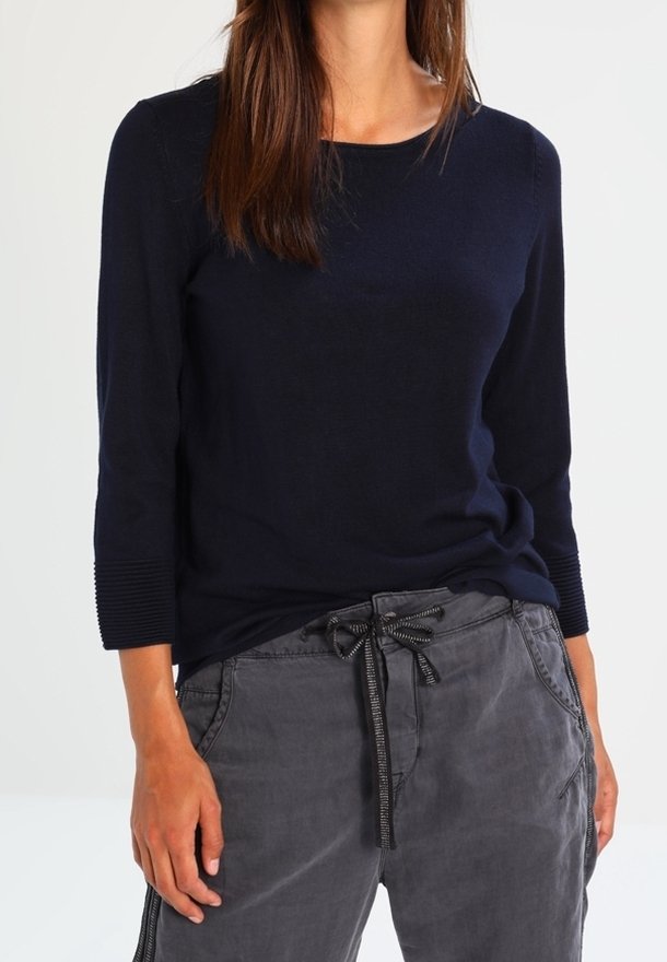 Laivastonsininen pitkähihoinen paita pyöreällä pääntiellä ja resoroiduilla hihojen resoreilla, yhdistettynä harmaisiin vetoketjullisiin housuihin, joissa on rento istuvuus.