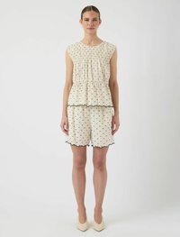 Top sin mangas color crema con textura fruncida y patrón de puntos negros, combinado con pantalones cortos a juego y bordes en forma de onda.