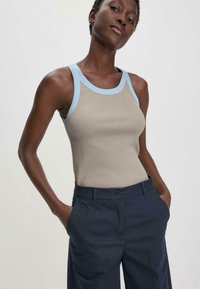 Beige ribbed tank top with light blue trim, paired with dark navy wide-leg trousers. The top features a round neckline and a fitted silhouette.