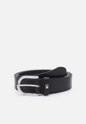 Ceinture en cuir noir roulée avec une boucle rectangulaire argentée brillante et un petit logo rouge, blanc et noir sur la boucle.