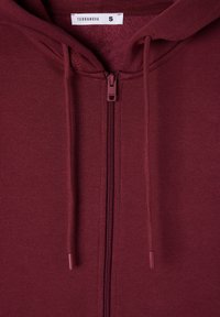 Felpa bordeaux con zip, cordini e una morbida fodera interna. Presenta un'etichetta del marchio sul collo e un design semplice e uniforme.