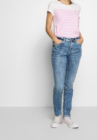 Vitt t-shirt med kort ärm och rosa ränder, kombinerat med blekta blå denimjeans. Sneakers kompletterar den avslappnade stilen.