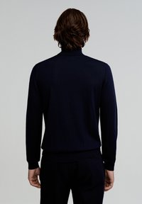 Marineblauer Rollkragenpullover mit langen Ärmeln, gerippter Textur, figurbetontem Design und kontrastierenden Bündchen. Minimalistischer Stil, keine sichtbaren Muster oder Beschläge.