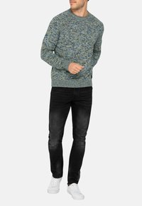 Maglione a maglia blu e verde con un motivo testurizzato, scollo rotondo e polsini a costine, abbinato a jeans neri e sneakers bianche.