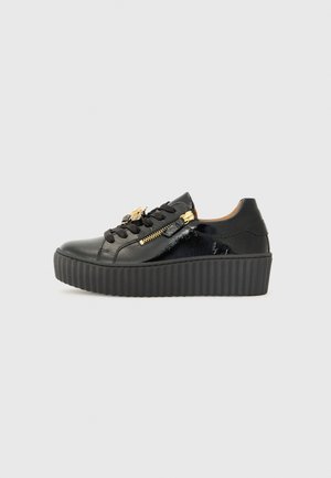 Sneaker in pelle nera con finitura lucida, design con lacci, zip laterale e suola piatta spessa e rigata. Accenti in metallo dorato.