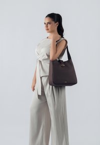 Borsa a mano in pelle marrone con superficie liscia e forma strutturata, dotata di manico corto e dettagli in metallo dorato.