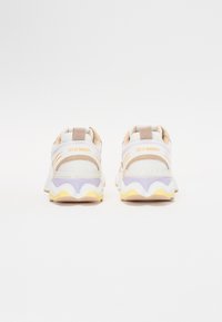 Sneaker bianchi in mesh con accenti beige, caratterizzate da una suola ondulata in lavanda e giallo, e un'etichetta sul retro con la scritta "Steve Madden".