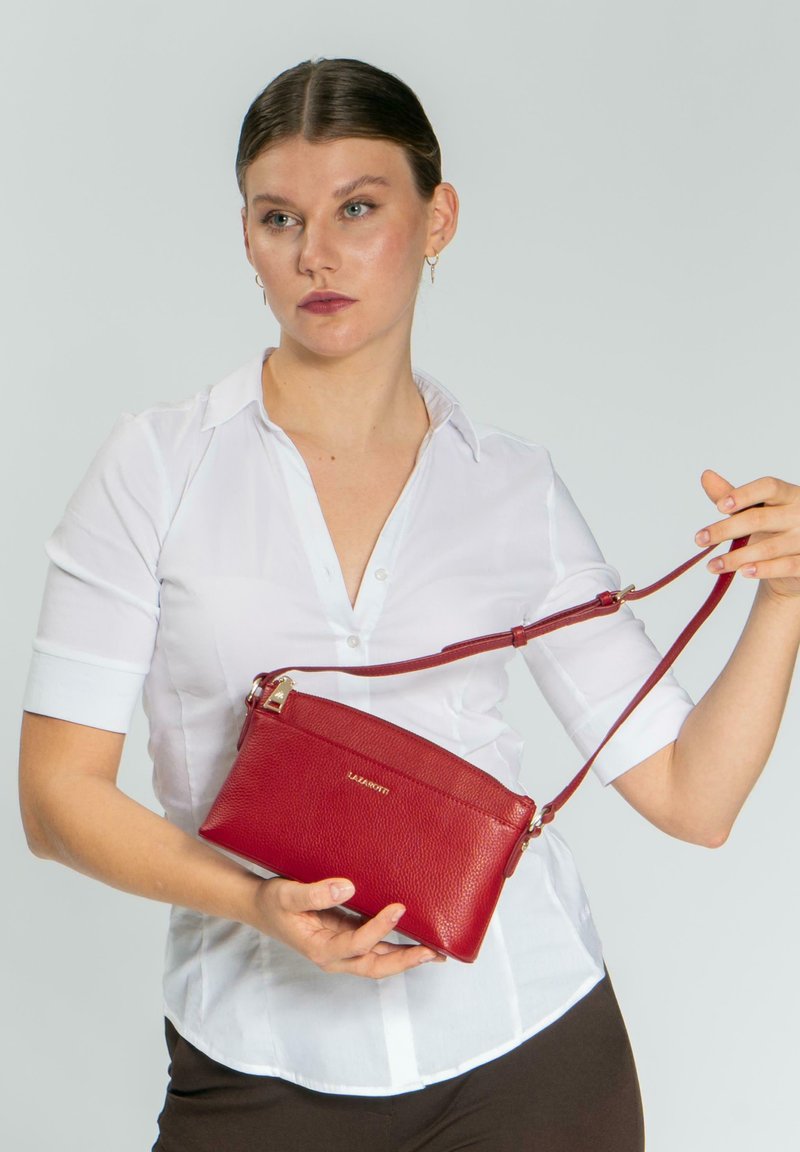 Borsa a tracolla rossa in pelle con superficie texturizzata, chiusura con zip e tracolla regolabile. Dettagli in oro su una forma rettangolare.