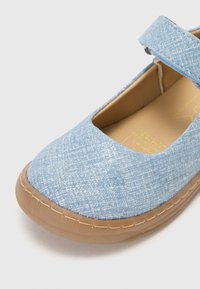 Chaussure Mary Jane en tissu bleu avec une surface texturée, bout rond, bride ajustable et semelle en caoutchouc beige. L'intérieur présente un logo jaune.