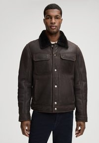 Brązowa skórzana kurtka z futrzanym kołnierzem, wyposażona w dwie kieszenie na piersi, kieszenie boczne oraz srebrne zatrzaski. Miękka tekstura i dopasowany krój.