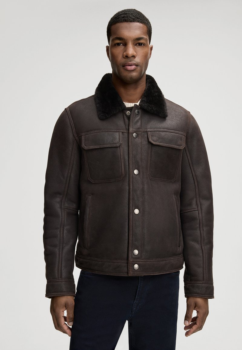 Brązowa skórzana kurtka z futrzanym kołnierzem, wyposażona w dwie kieszenie na piersi, kieszenie boczne oraz srebrne zatrzaski. Miękka tekstura i dopasowany krój.